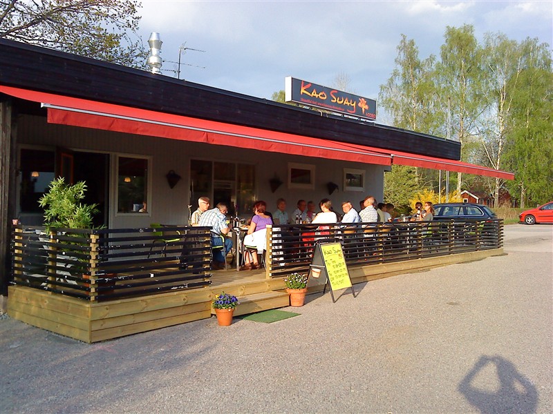 Restaurangen utifrån med röd markis och uteservering på trädäck
